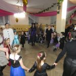 Grupa dzieci i dorosłych tańcząca w strojach karnawałowych na sali.