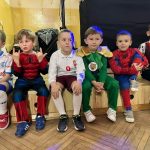 Grupa sześciu chłopców strojach karnawałowych siedząca na podeście w sali.