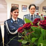 Dwie kobiety ubrane w mundury policyjne. Przed nimi osoba trzymająca bukiet róż,