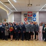 Grupa osób w oficjalnych stroajach i mundurach stojąca na sali konferencyjnej pozuje do fotografii.