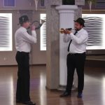 Dwóch mężczyzn w czarnych spodniach, białych koszulach grająca na trąbkach.