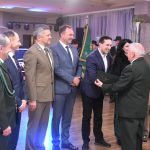 Grupa osób w garniturach i uroczystych strojach. Starszy mezczyzna składa im gratulację.