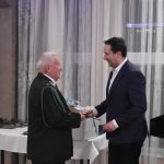 Dwóch mężczyzn w garniturach. Młodszy składa starszemu gratulację.