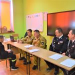 Czterech mężczyzn w garniturach siedzi przy długim stole i egzaminuje młodego chłopca.