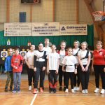 Kobieta w czerwniej koszuli i grupa młodzierzy w łuczniczych strojach sportowych pozujacych do zdjęcia.