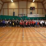 Grupa osób (głównie dzieci i młodzieży) w łuczniczych strojach sportowych na sali gimnastycznej.