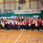 Duża grupa osób (głównie dzieci i młodzieży) w łuczniczych strojach sportowych na sali gimnastycznej.