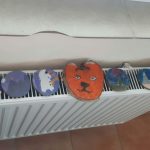 Na białym grzejniku leżą kolorowe prace z drzewa.