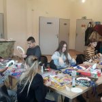 Grupa dzieci siedzi prz stoliku i wycina z papieru różne rzeczy.