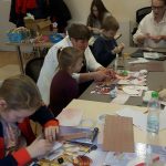 Grupa dzieci siedzi prz stoliku i wycina z papieru różne rzeczy.