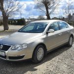 Duże srebrne auto na żwirowym placu w słoneczny dzień.