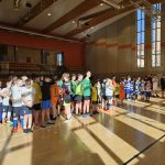 Grupa młodych zawodników - piłkarzy ustawiona w rzędzie na sali gimnastycznej.