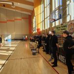 Grupa dorosłych i dzieci ustawiona na sali gimanstycznej. W centrum zdjecia widać stolik z nagrodami.