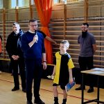 Grupa dorosłych mężczyzn z młodym zawodnikiem trzymajacym statuetkę oraz dyplom.