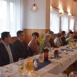 Grupa kobiet i mężczyzn siedzaca na rozległej sali przy podłuznym stole.