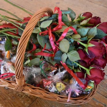 Bukiet róż i słodecze w wiklinowym koszu.