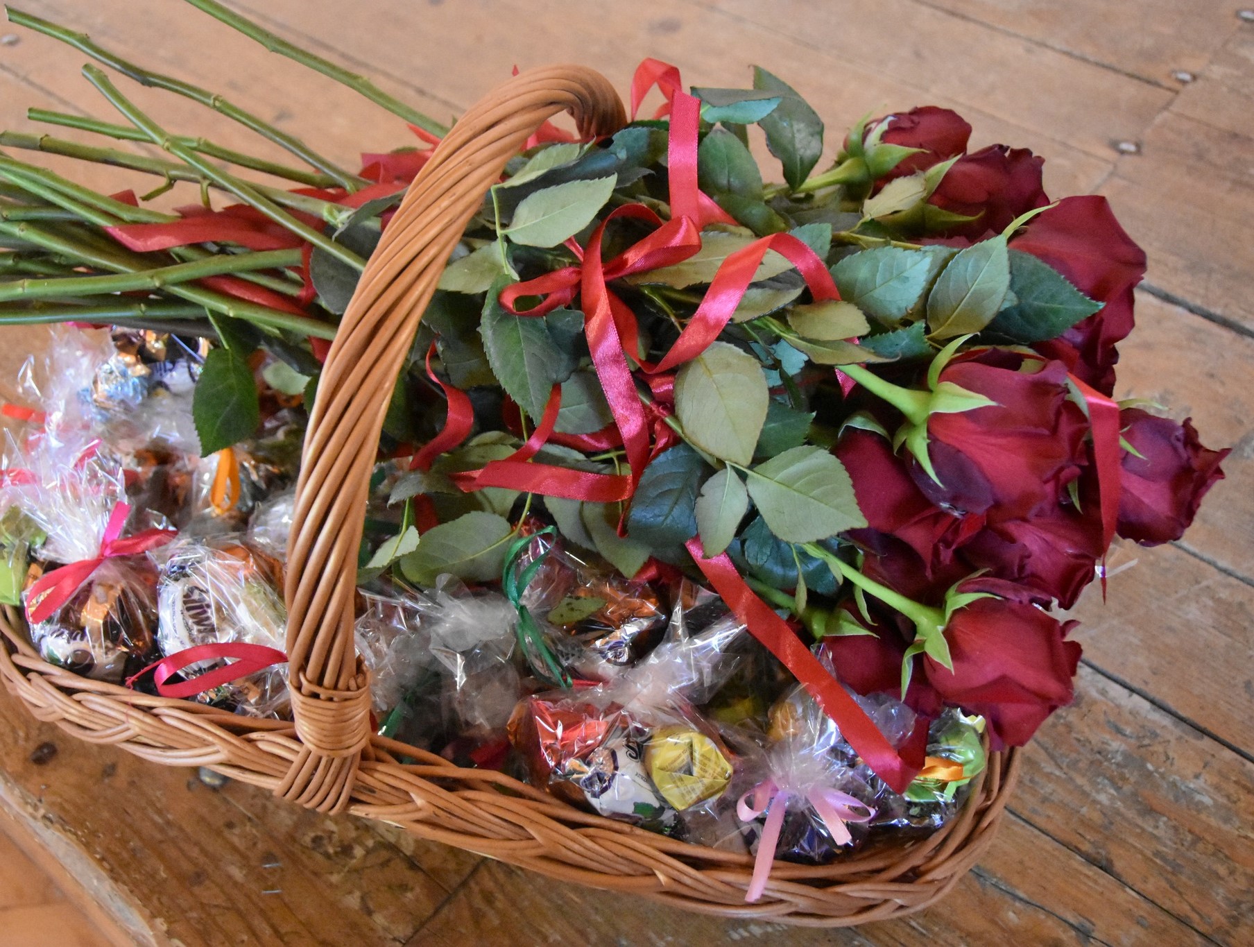 Bukiet róż i słodecze w wiklinowym koszu.