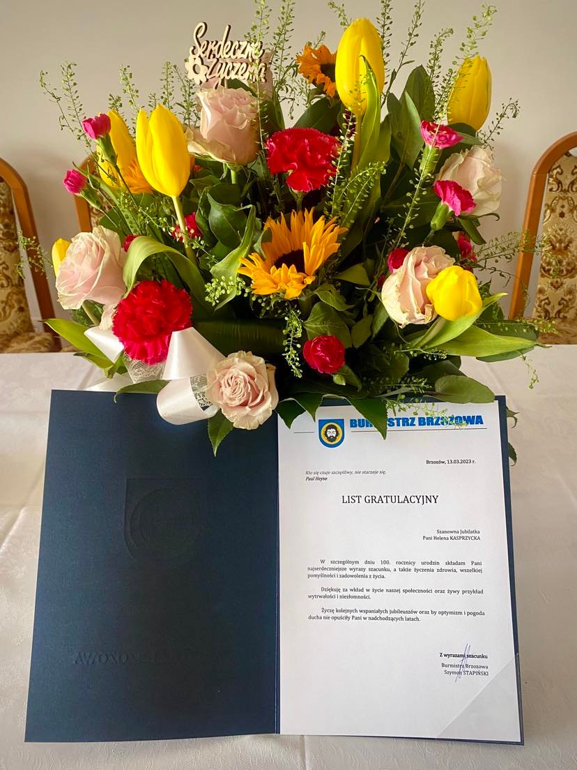 List gratulacyjny i bukiet kwaitów położone na stole.