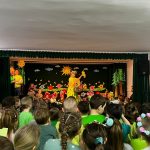 Grupa dzieci oglądajaca przedstawienie teatralne na rozleglej sali. W centrum kobieta w stroju wisony.