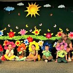 Grupa dzieci w stroju kwiatow. Przy nich znajduje sie opiekunka.