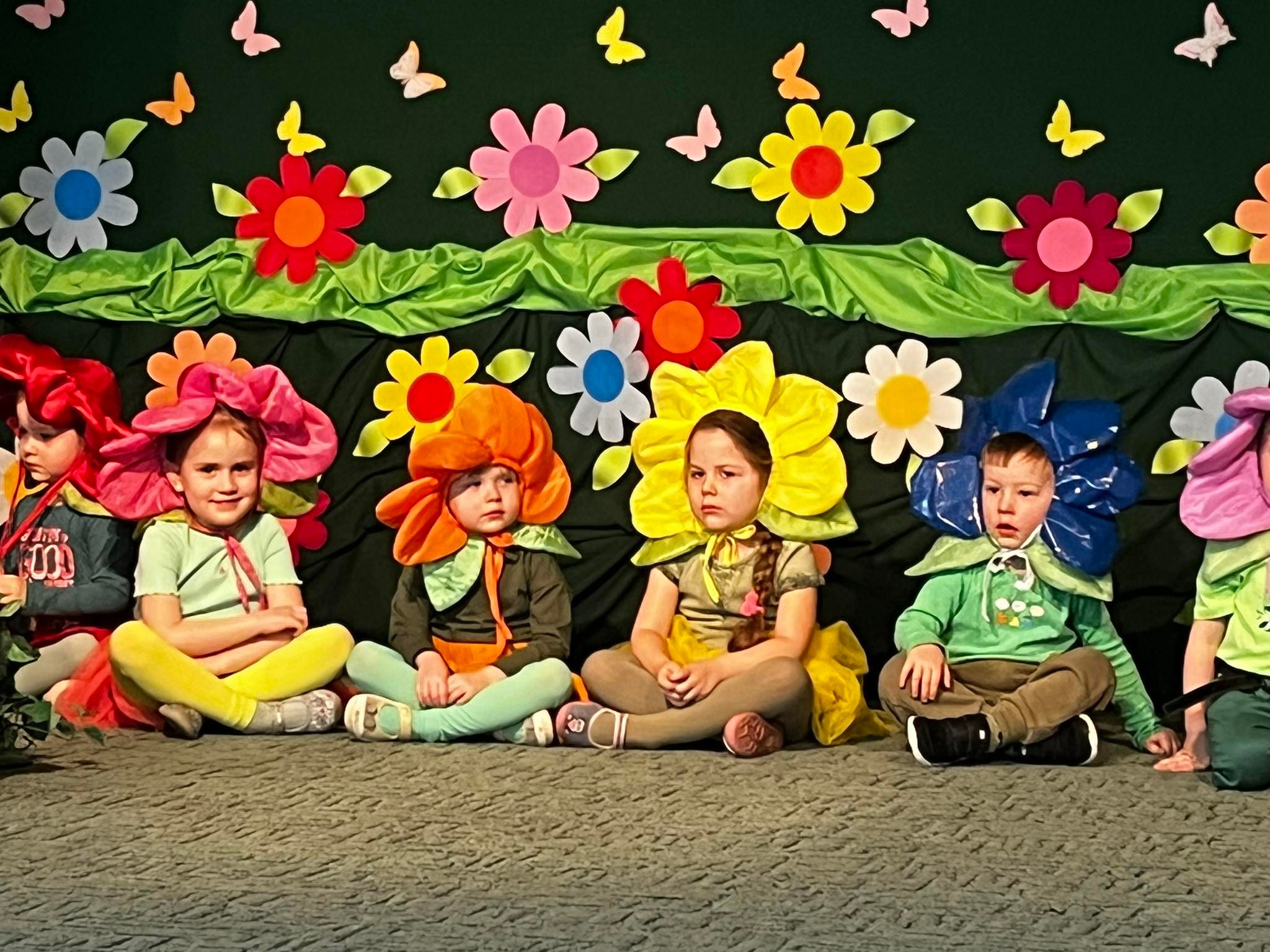 Kilkoro dzieci w stroju kwaitów siedzaca na scenie.