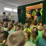 Grupa dzieci oglądajaca przedstawienie teatralne na rozleglej sali.