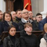 Grupa osób rożnej płci i wieku zasiadających w drewnianych ławkach kościelnych.