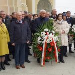 Grupa dorosłych osób stojąca na zewnątrz z biało-czerwonymi wieńcami.