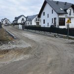 Utwardzona droga bez powierzchni asfaltowej obok domów mieszkalnych.