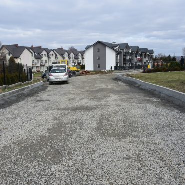 Utwardzona droga bez powierzchni asfaltowej obok zabudowy szeregowej.