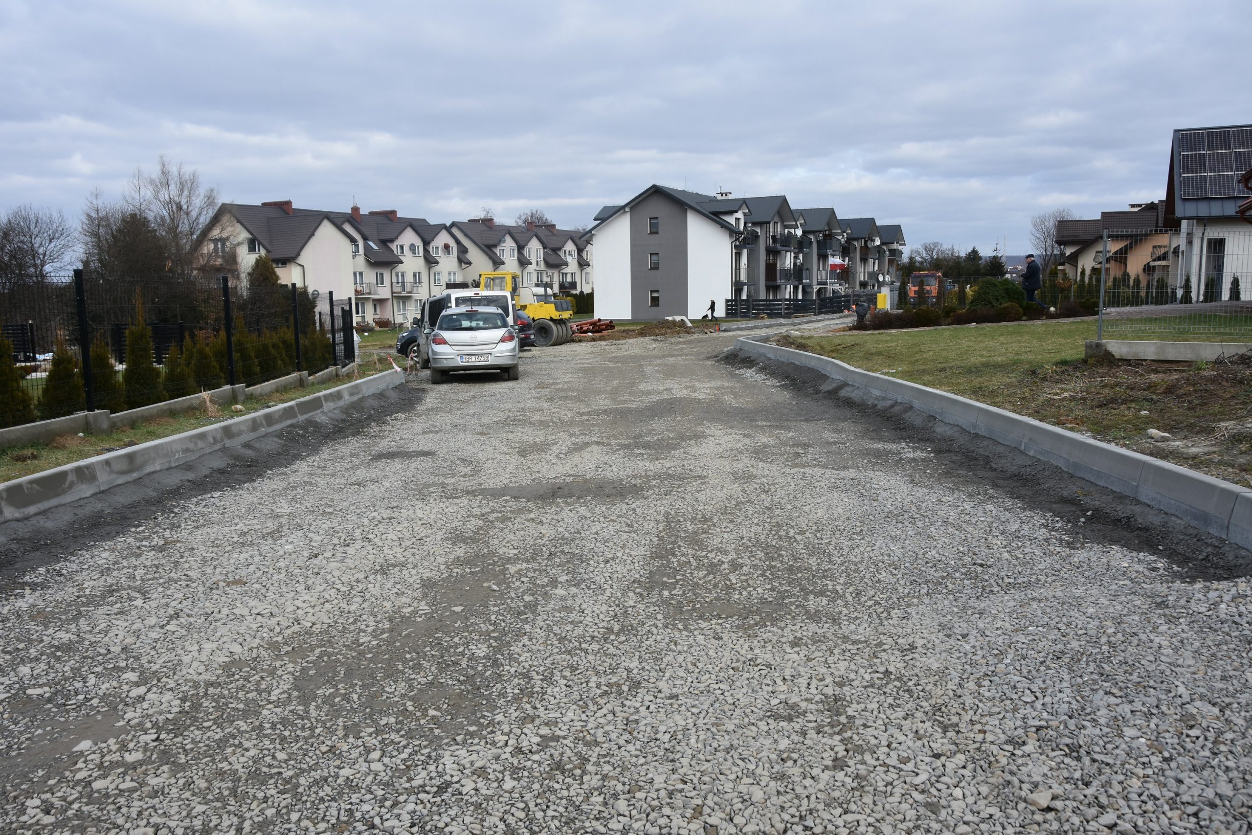 Utwardzona droga bez powierzchni asfaltowej obok zabudowy szeregowej.