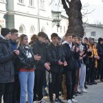 Grupa młodzieży stojąca na chodniku w słoneczny dzień.