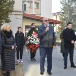 Grupa dorosłych i młodzieży stojacych przed gmachem urzędu. Starszy mężczyzna przemawia za pomocą mikrofonu.