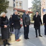 Grupa dorosłych i młodzieży stojacych przed gmachem urzędu. Młody mężczyzna przemawia za pomocą mikrofonu.