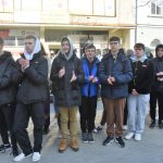 Grupa młodzieży stojąca na chodniku w słoneczny dzień.