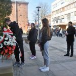 Grupa młodzieży i dwójka mężczyżn skłądajacych wieniec i znicze przed popiersiem Piłsudskiego.