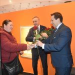 Dwóch mężczyzn w graniturach przekazuje kobiecie róże.