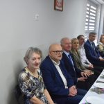 Grupa elegancko ubranych dorosłych zasiadająca przy podłużnym stole.