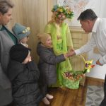 Starszy mężczyzna w białej koszuli wita sie z dzieckiem. W tle dwie kobiety i grupa dzieci.