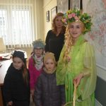 Młoda kobieta w ciemnej koszuli pozuje do zdjecia z grupą dzieci i kobietą ubraną w strój reprezentujacy wiosnę.