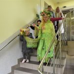 Grupa dzieci i kobiet schodząca ze schodów. Jedna z kobiet ubrana jest w strój reprezentujący wiosnę.