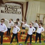 Grupa chłopców w białych koszulach i ciemnych spodniach i okularach w czasie występu tanecznego.