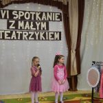 Dwie dziewczynki w czasie wystepu teatralnego. Obok stoi wieszak z ubraniami.