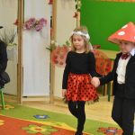 Chłopczyk w stoju muchomora i dziwczynka w stoju biedronki. Obok siedzi kobieta ubrana w strój czarownicy.