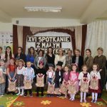 Grupa dorosłych i dzieci ubranych w stroje potaci z bajek pozujacych do wspólnego zdjecia na salce szkolnej.