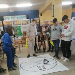 Grupa młodzieży w czasie zawodów robotów. Jeden z chłopców obsługuje małego robota.