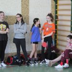 Grupa młodych dziewcząt siedząca i stojącana sali gimanstycznej.