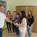 Rozdanie dyplomów grupie dziewcząt. Męzczyzna w białej koszuli przekazuje dyplom dziewczynie w białej koszuli.