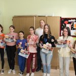 Rozdanie dyplomów grupie dziewcząt. Mężczyzna w białej koszuli pozuje do zdjecia z laureatkami w szkolnej klasie.