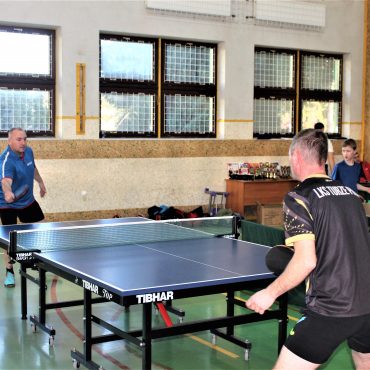 Dwóch mężczyzn na sali gimanstycznej grajacy w tenis stołowy.